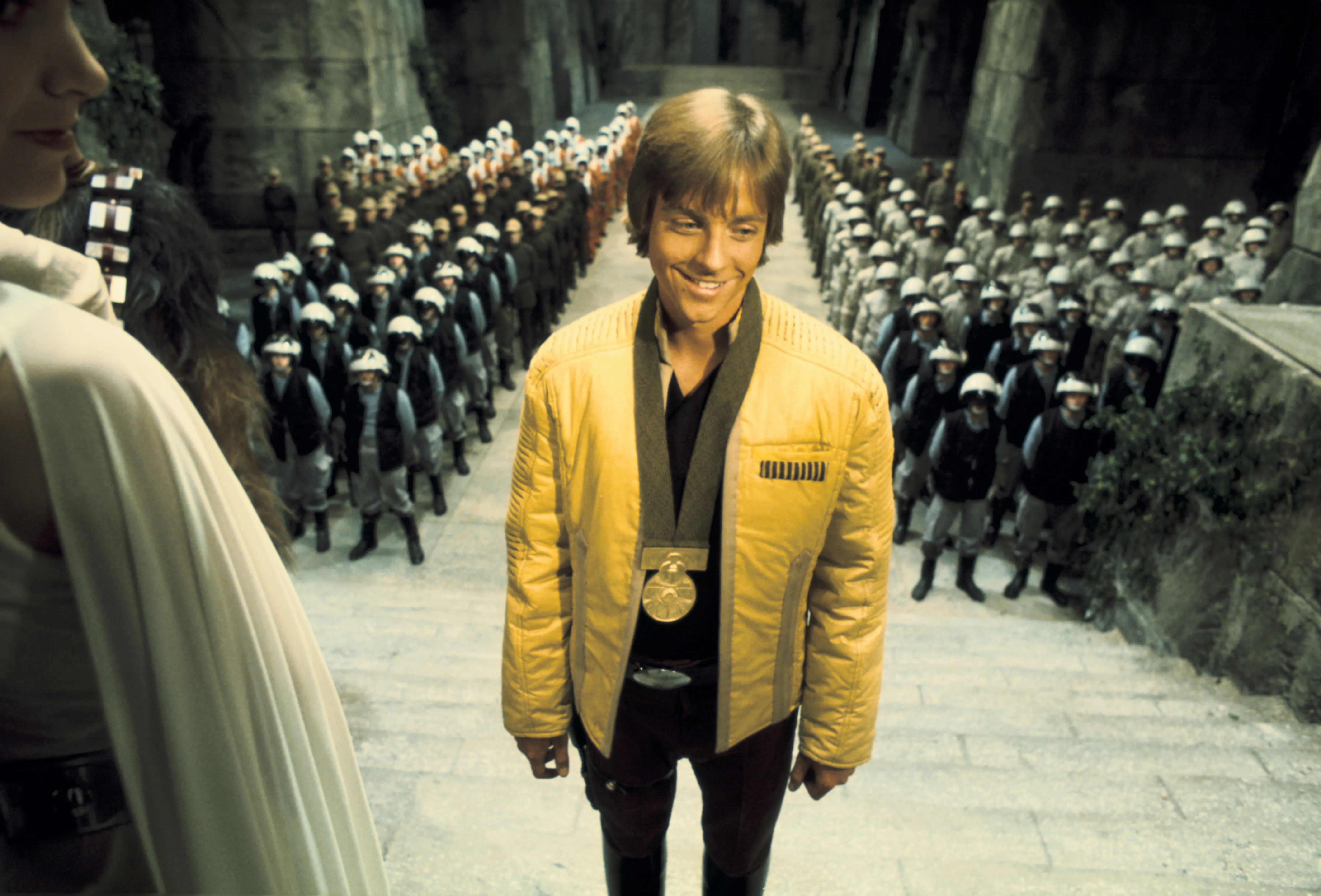 Ein junger Mann in einer goldenen Jacke in einem überfüllten Thronsaal.