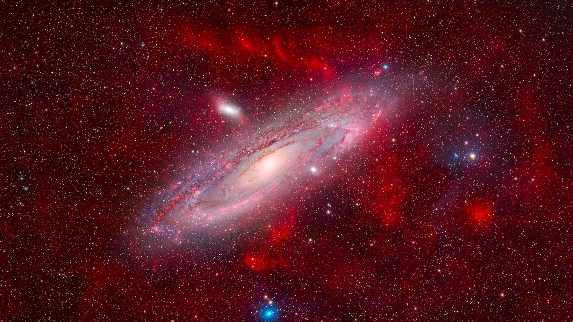 eine weiße, wolkige Spirale in der Mitte des Bildes ist von roten Gaswolken umgeben. Tausende von Sternen sind im Hintergrund zu sehen
